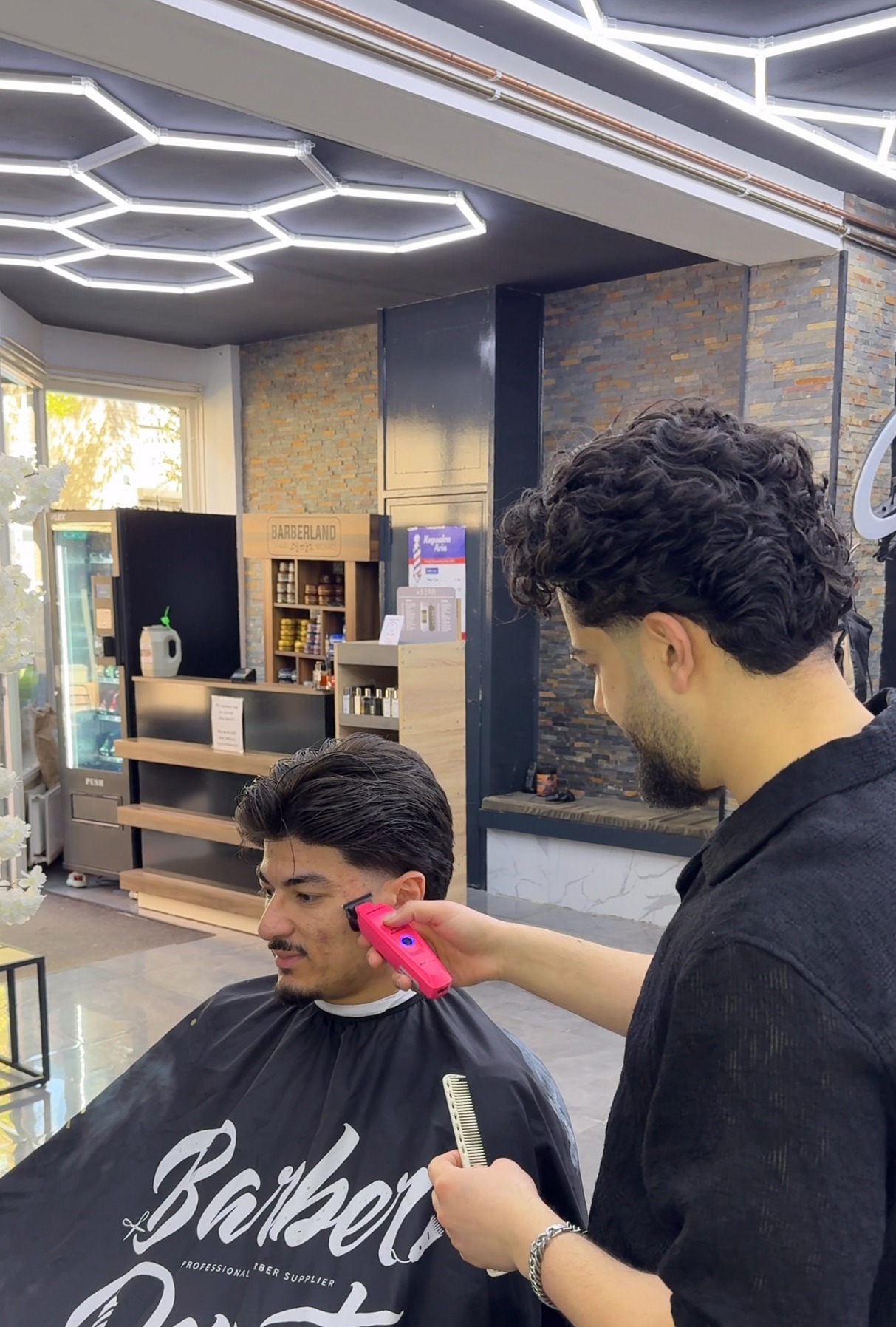 Barbier met roze tondeuse onder het zeshoekige lichtplafond van de shop